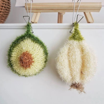 Two avocado-shaped and garlic-shaped dish scrubbers hanging on a wooden rod against a white wall.
